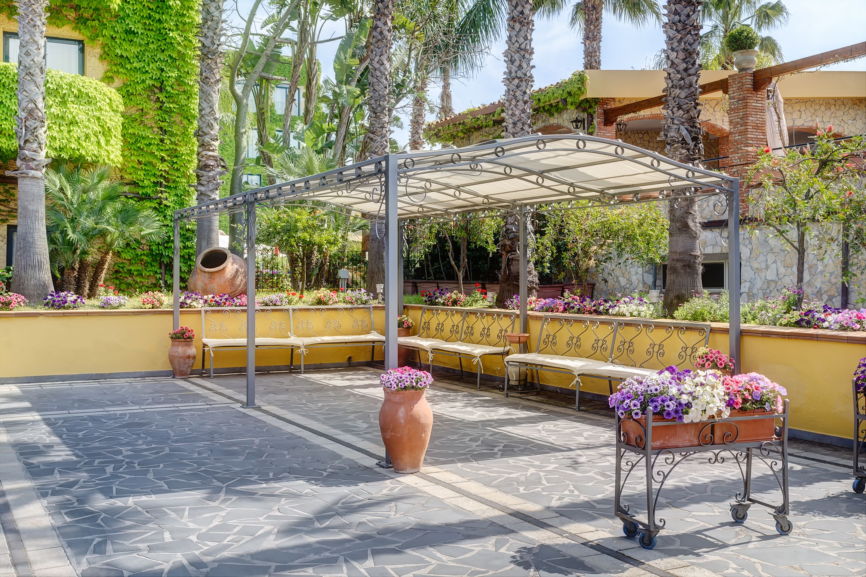 Ein überdachter Außenbereich mit Pergola, Bänken und Blumenkübeln.