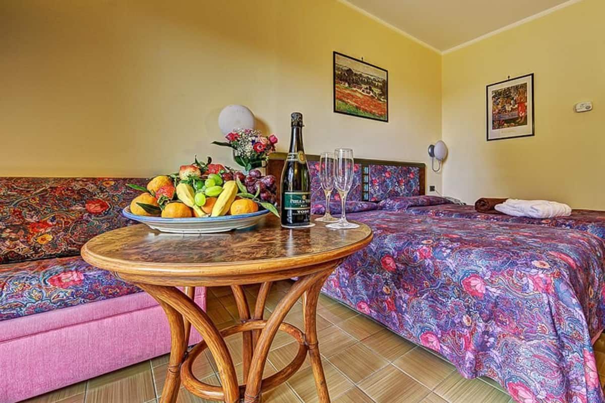 Une chambre d’hôtel avec un lit, une table ronde sur laquelle se trouvent un panier de fruits et une bouteille, et un canapé.