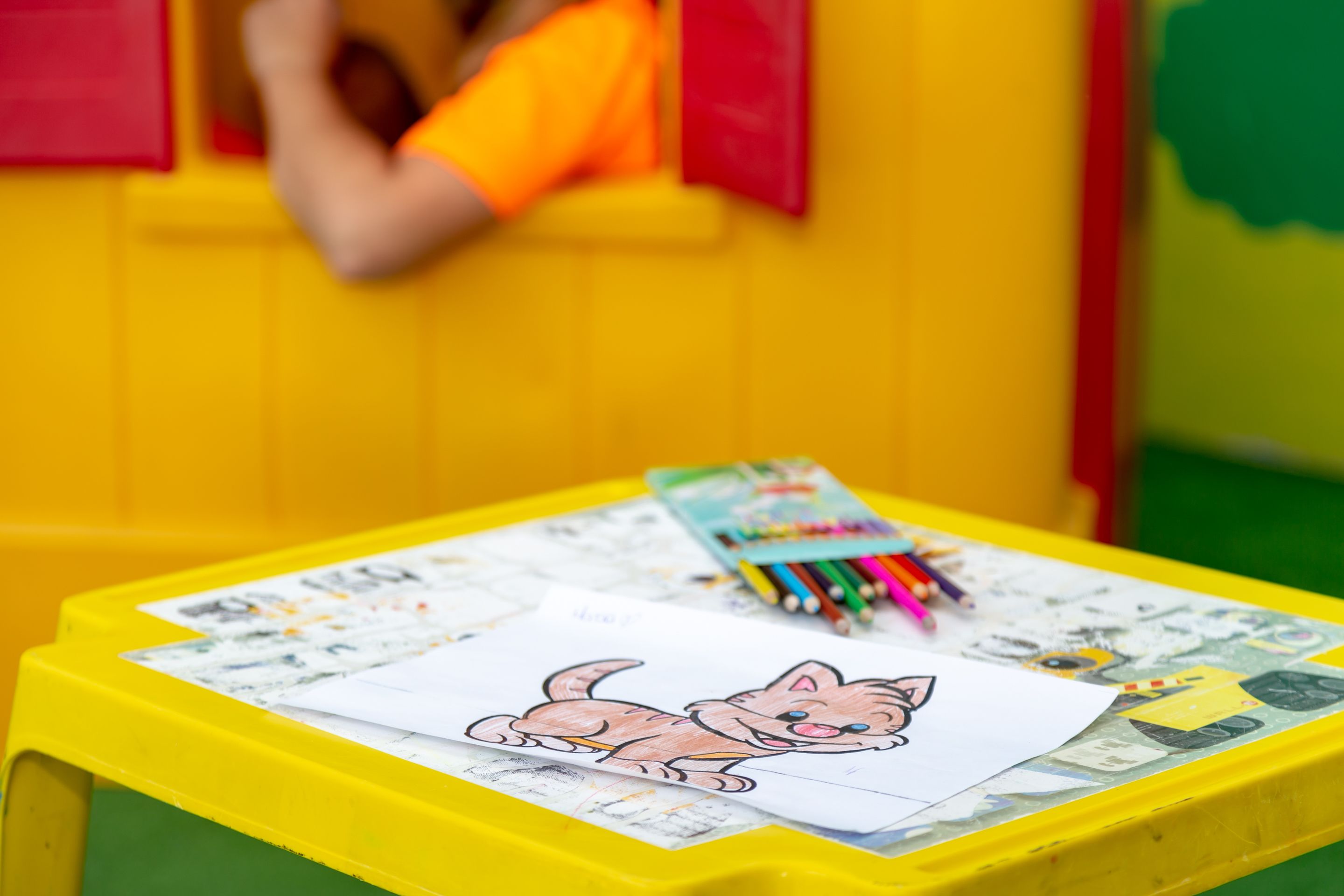 A yellow table with a drawing of a cat, colored pencils, and a coloring book.