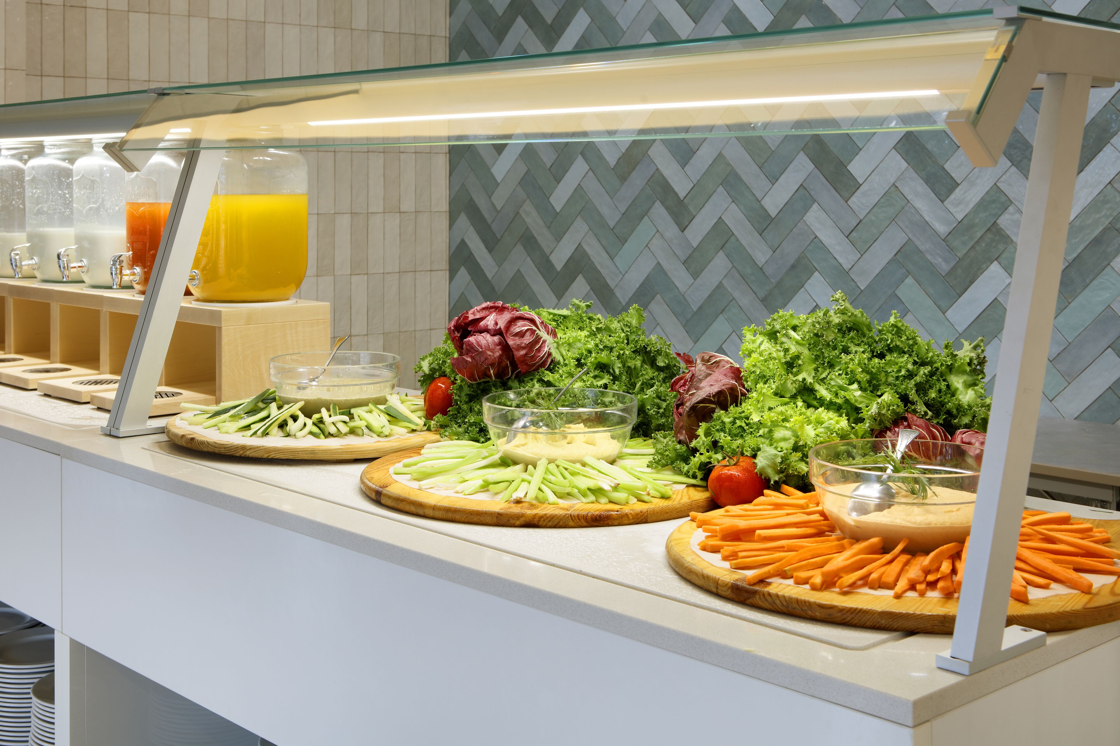 Un bufé con diferentes opciones de comida, incluyendo verduras, frutas y un vaso de jugo de naranja.