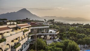 A multi-story hotel with balconies, outdoor seating, and a view of a mountain and sea. - Grand Palladium Sicilia Resort & Spa  (Campofelice di Roccella)