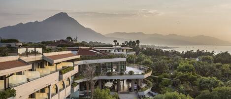 A multi-story hotel with balconies, outdoor seating, and a view of a mountain and sea.