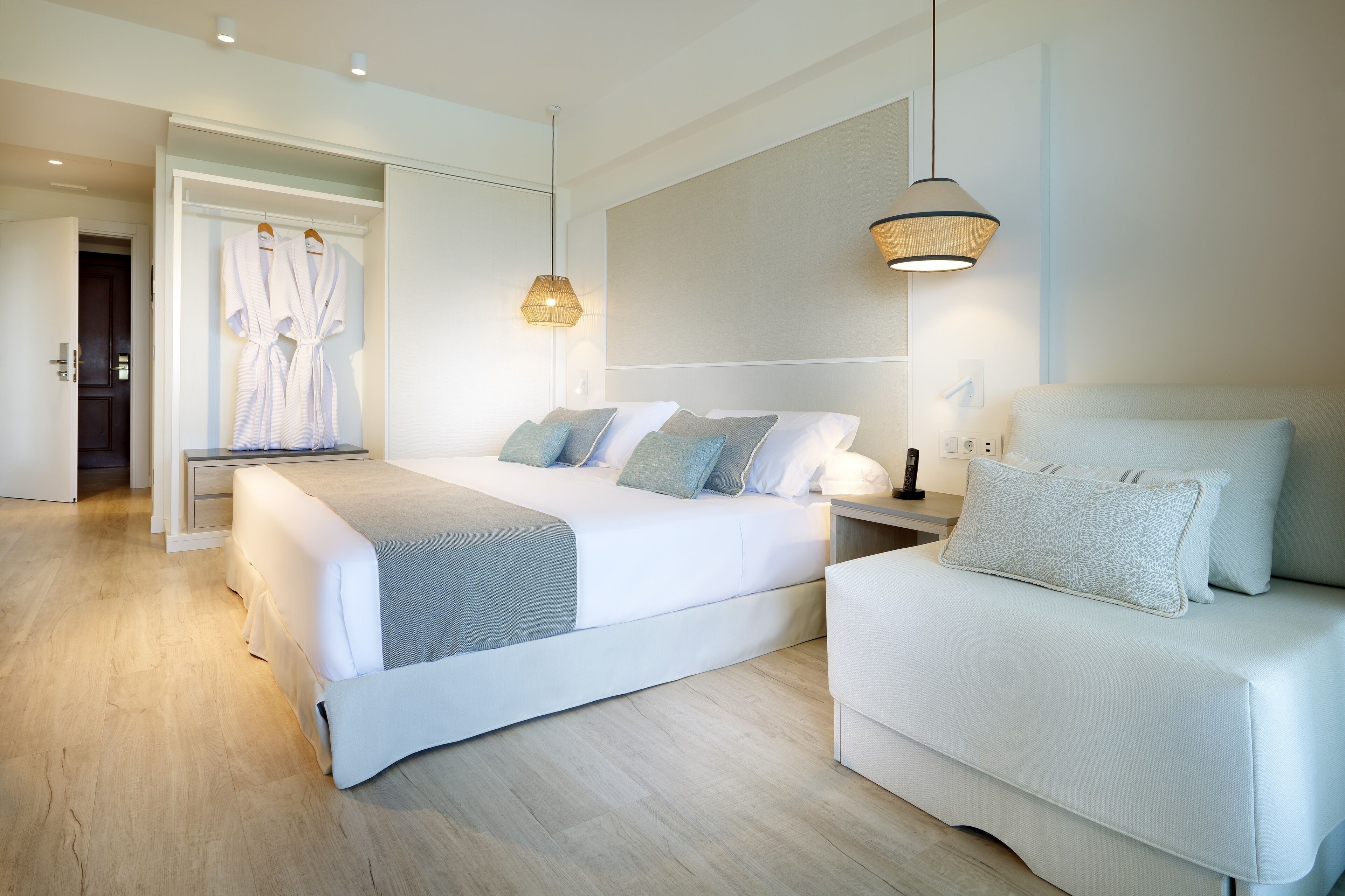Een moderne slaapkamer met een groot bed, nachtkastjes, een sofa en een inloopkast met aanhangende jassen.