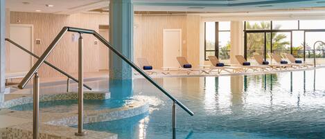 A swimming pool with a tiled deck and a metal handrail, surrounded by lounge chairs.