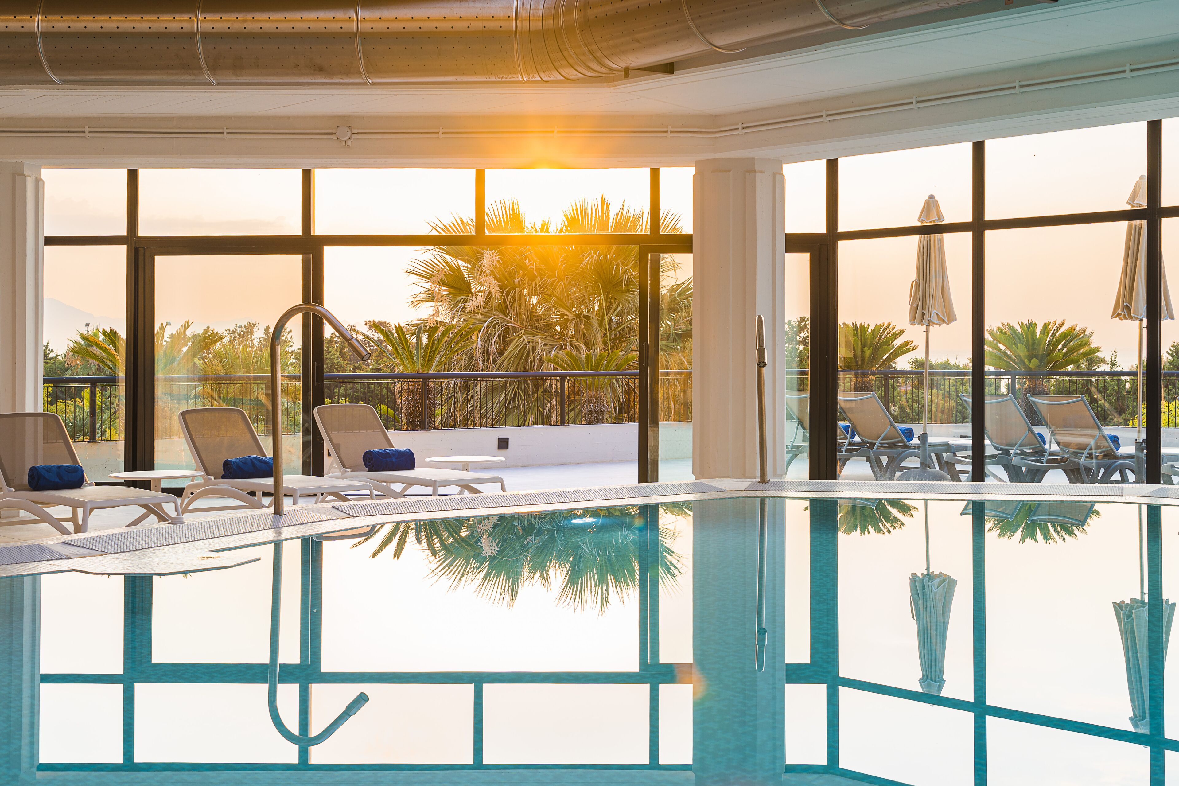 A swimming pool with lounge chairs and umbrellas, large windows with a view of palm trees and mountains.