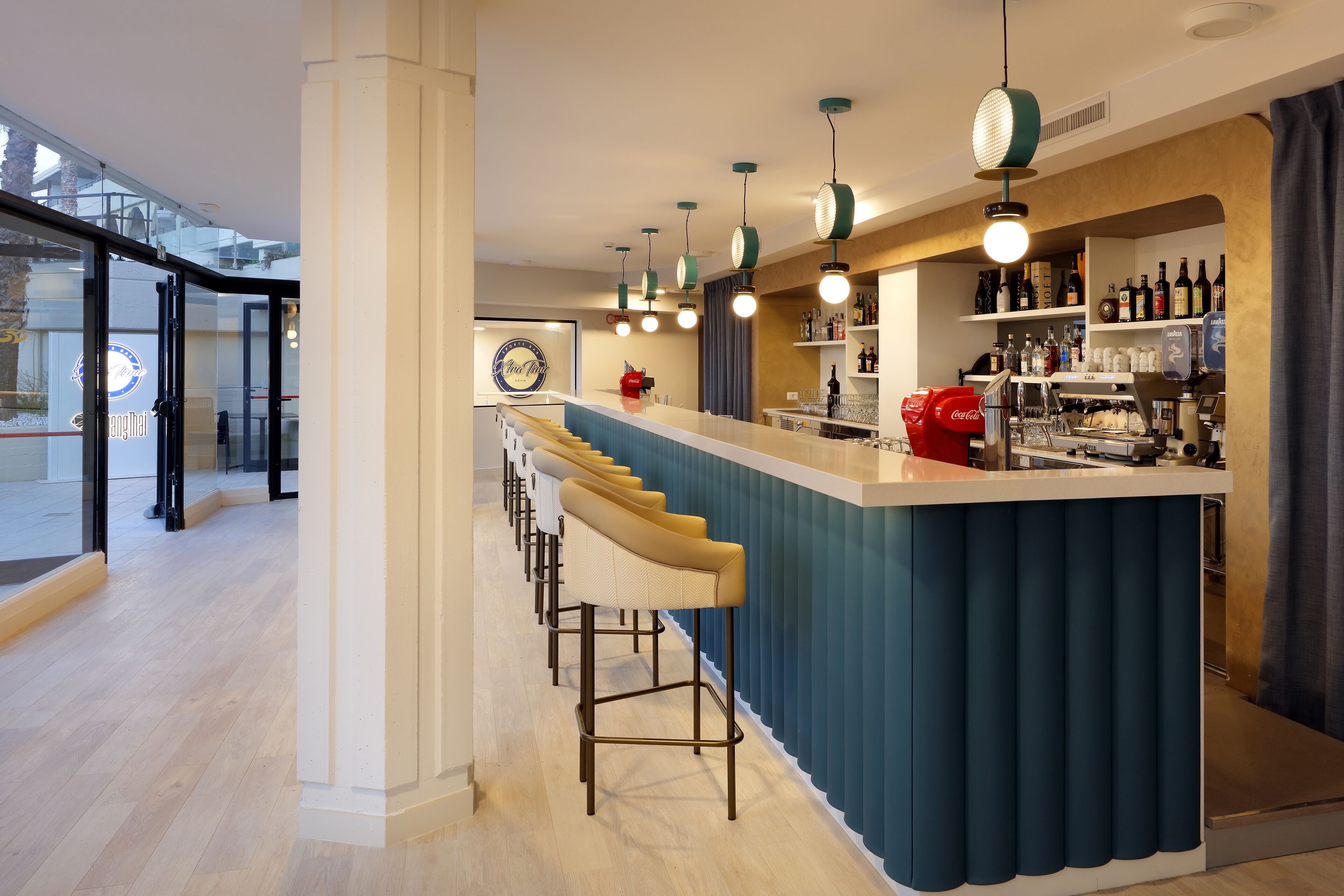 Zona de bar moderna amb taulell, tamborets i llums penjants.