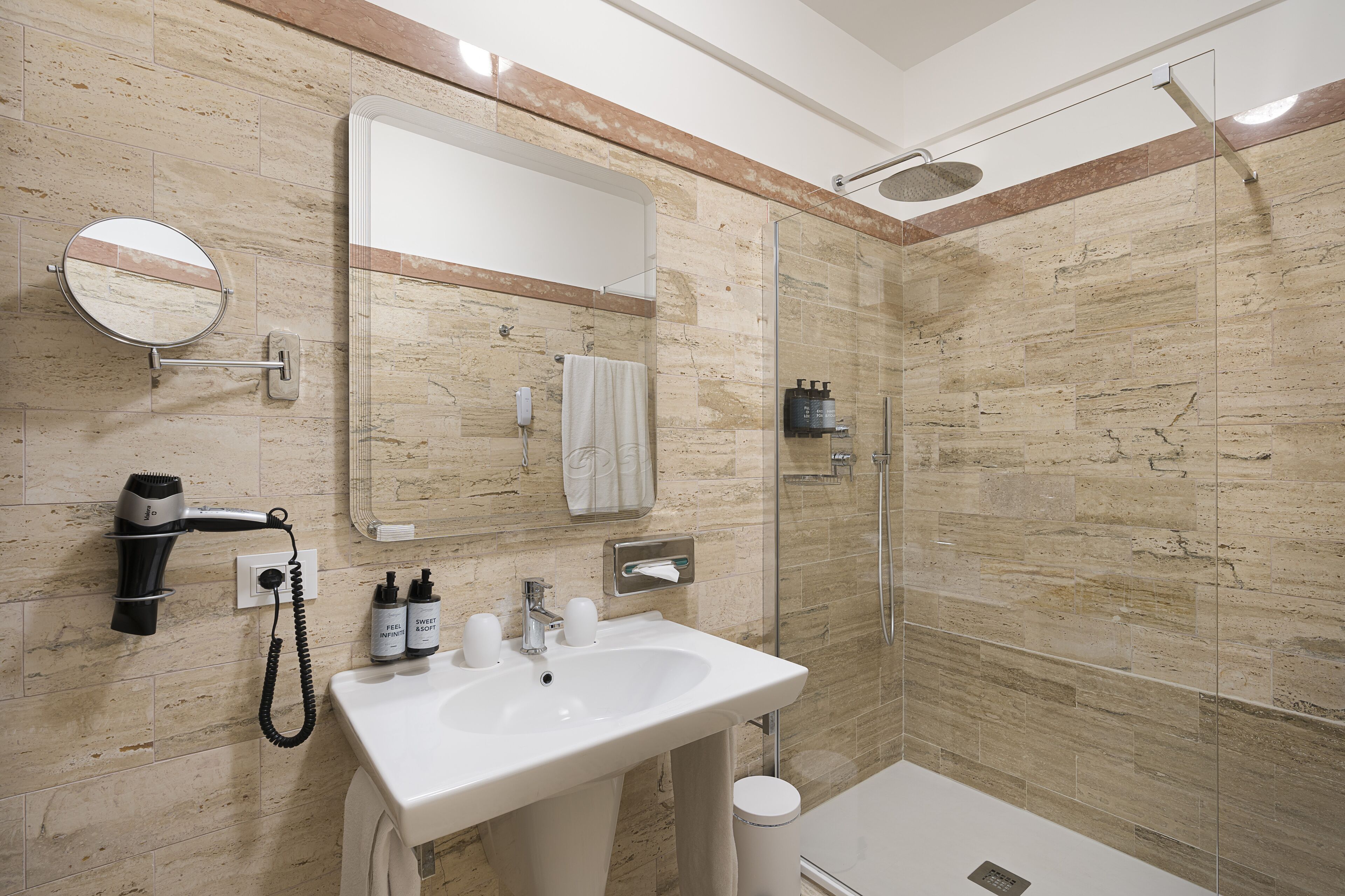 Een moderne badkamer met een grote spiegel, een wastafel, een douchecabine van glas en een haardroger aan de muur.