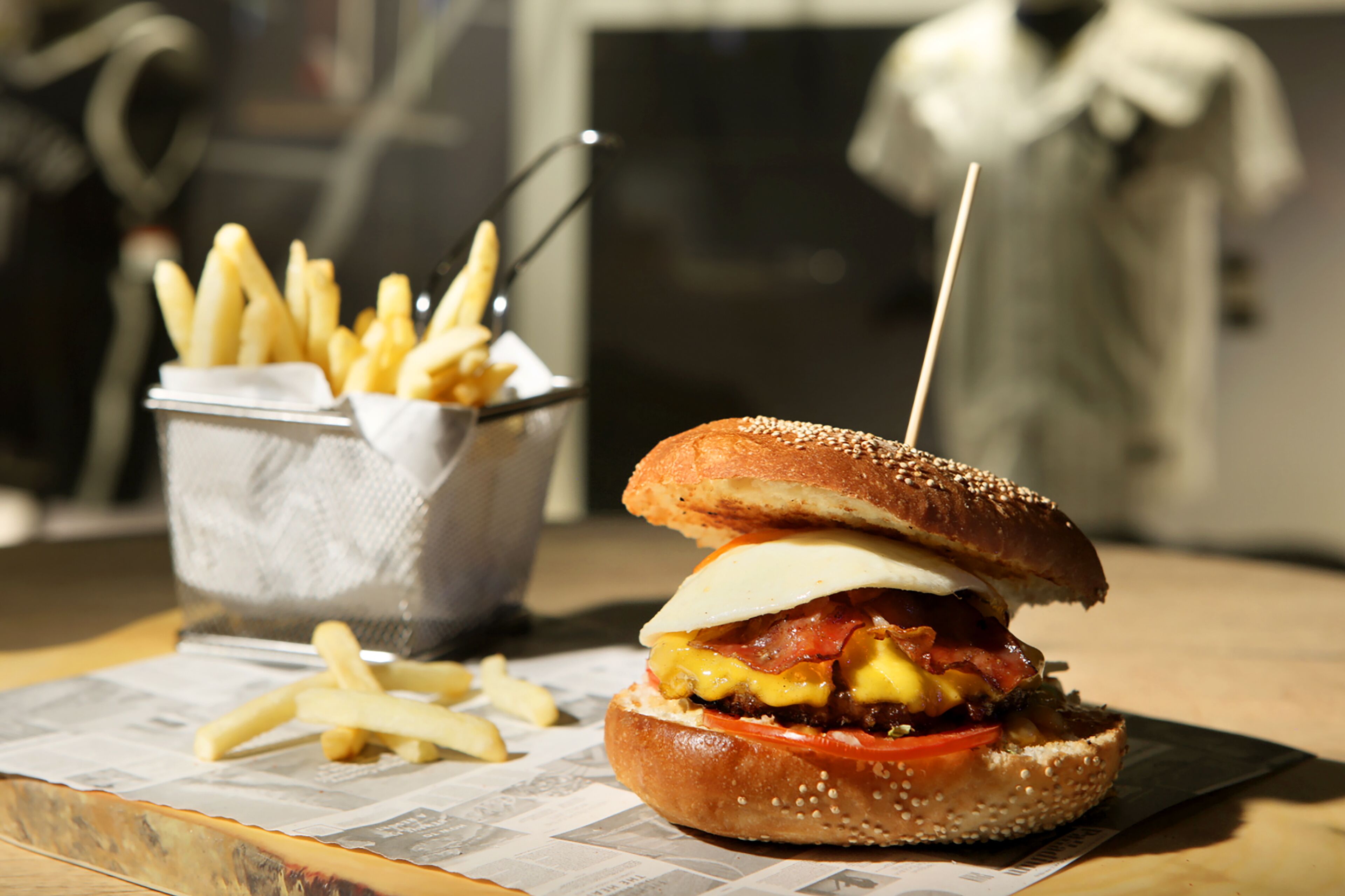 Un hamburger servi dans un pain aux graines de sésame, garni de fromage, de bacon et d’une tranche de tomate, accompagné d’une petite portion de frites.