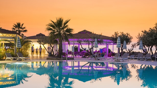A poolside area with lounge chairs and umbrellas, a covered seating area, and palm trees. - Grand Palladium Sicilia Resort & Spa  (Campofelice di Roccella)