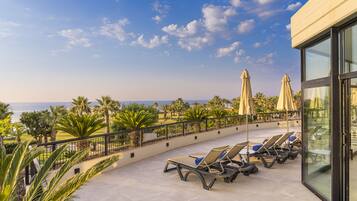 Terraza en la azotea con sillones y sombrillas, con vistas a una playa y palmeras.