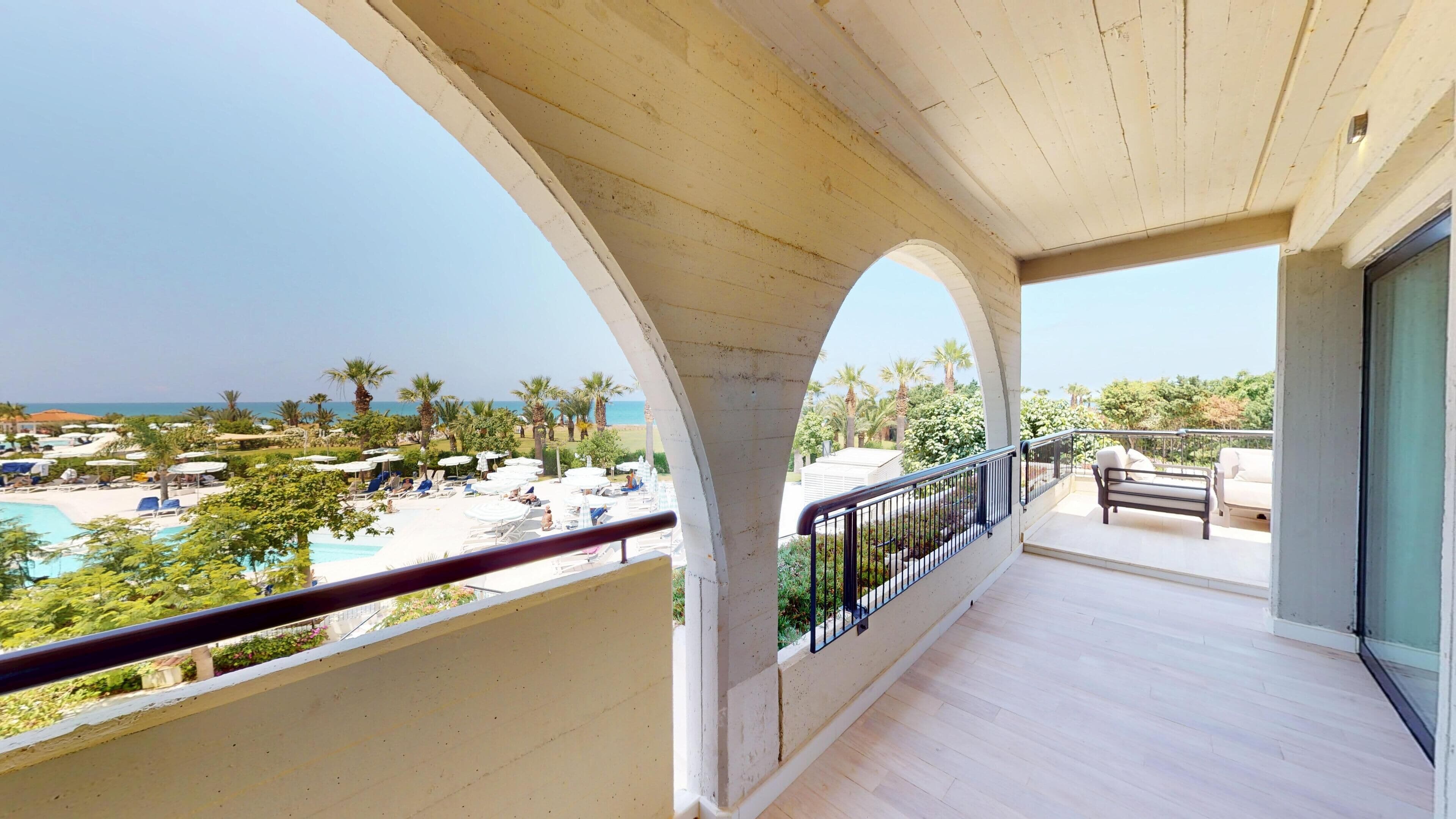 Un balcon avec vue sur une piscine et une plage, doté d’un plancher en bois et d’une balustrade.