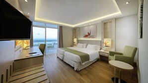 Una habitación de hotel moderna con una cama grande, un escritorio, una silla y una mesita. Tiene un balcón con vistas al océano.