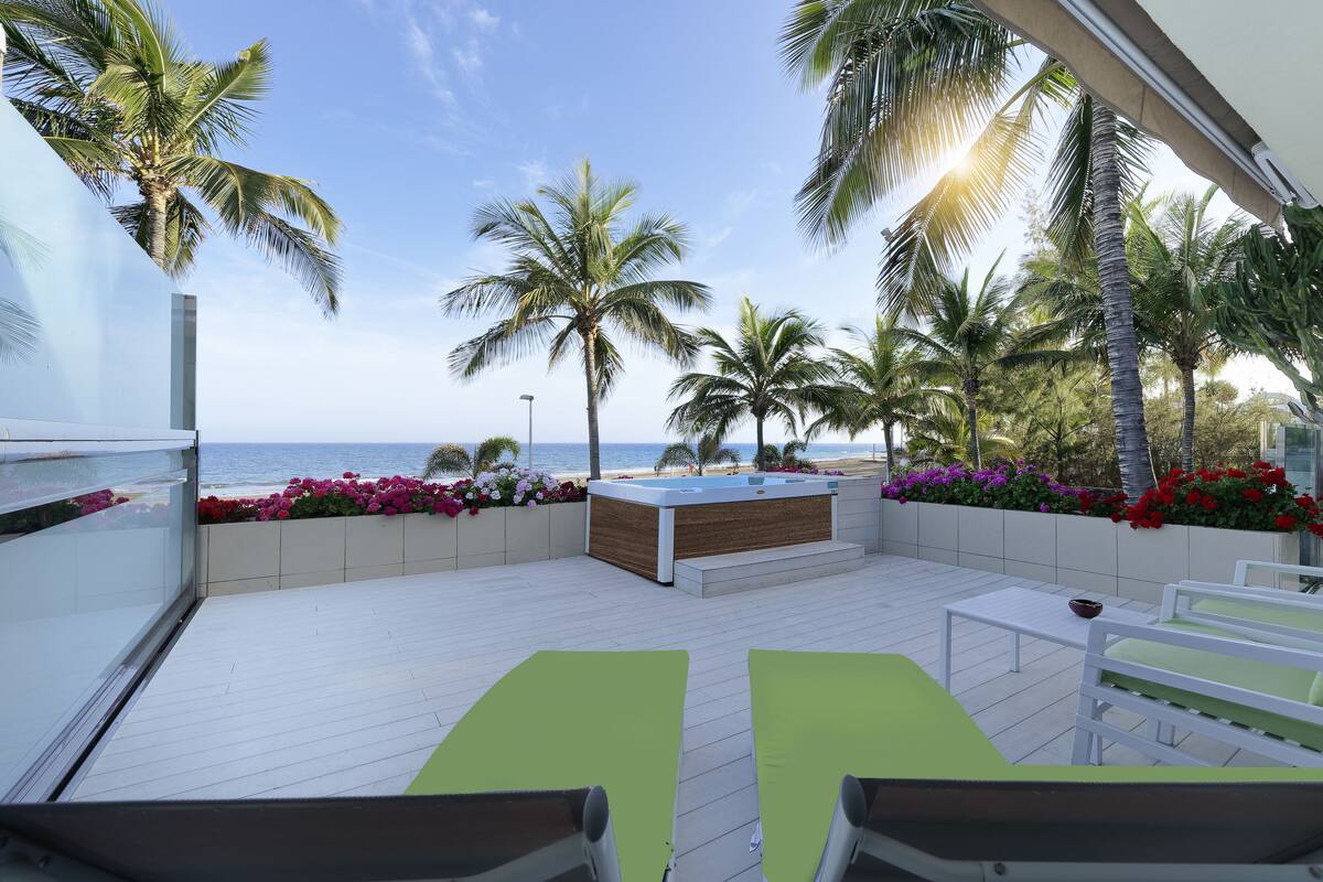 A balcony with a view of the sea, equipped with a hot tub, seating, and flower beds.