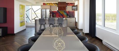 A modern kitchen with a central island, a dining area with a long table and chairs, and large windows providing natural light.