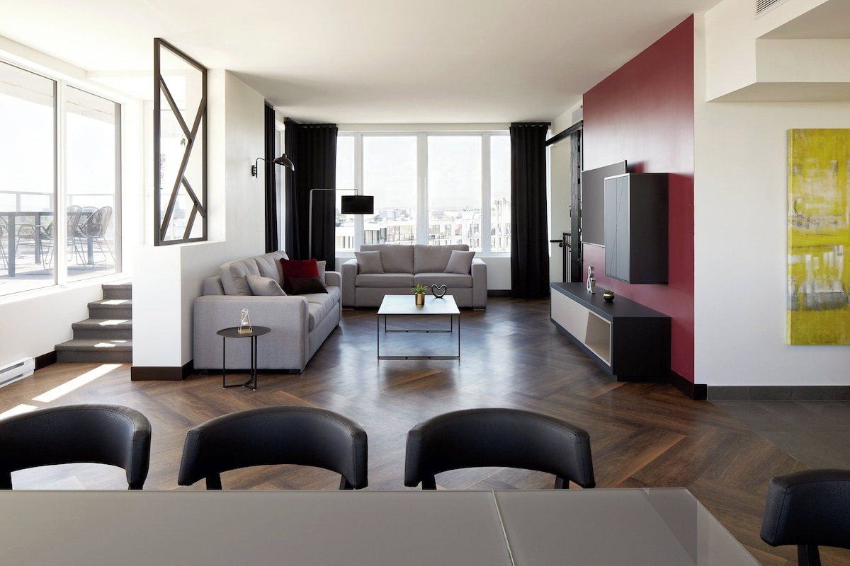 A modern living room with a sofa, coffee table, and chairs. There is a TV and artwork on the wall.