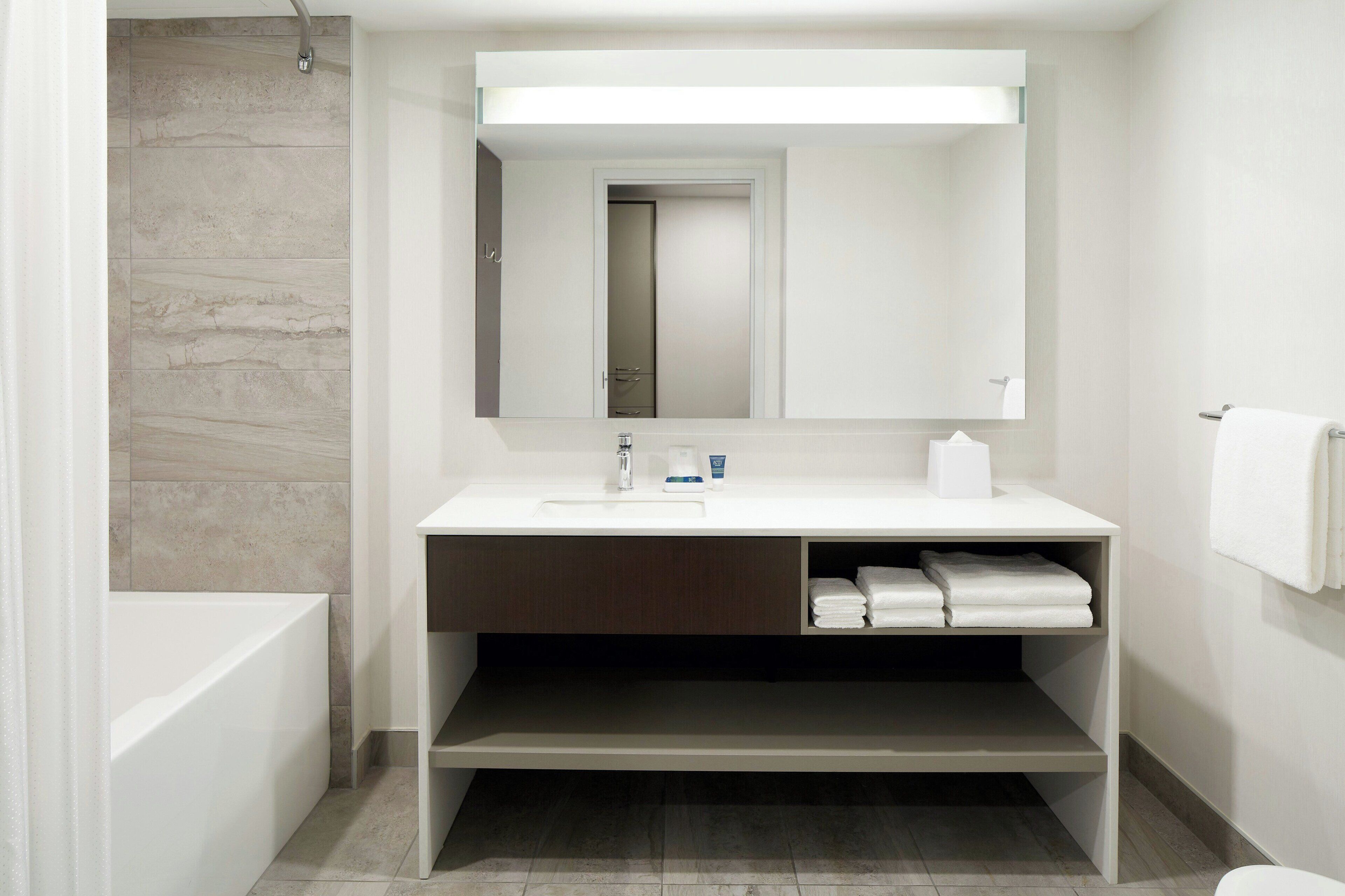 A modern bathroom with a bathtub, a sink with a mirror above it, and a towel rack on the wall.