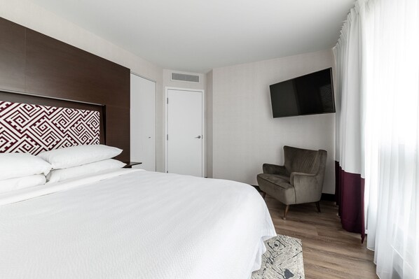 A hotel room with a large bed, a television mounted on the wall, a chair, and a door. - Four Points by Sheraton Levis Convention Centre (Levis)