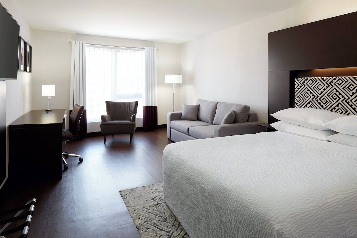A hotel room with a large bed, a sofa, a desk, and a chair.