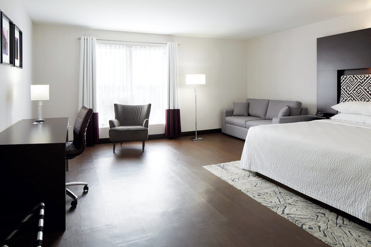 A modern hotel room with a large bed, a desk, a chair, a sofa, and a floor lamp.
