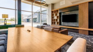 A modern conference room with a large wooden table, comfortable seating, a mounted TV, and a view of the outdoors through large windows. - Four Points by Sheraton Levis Convention Centre (Levis)