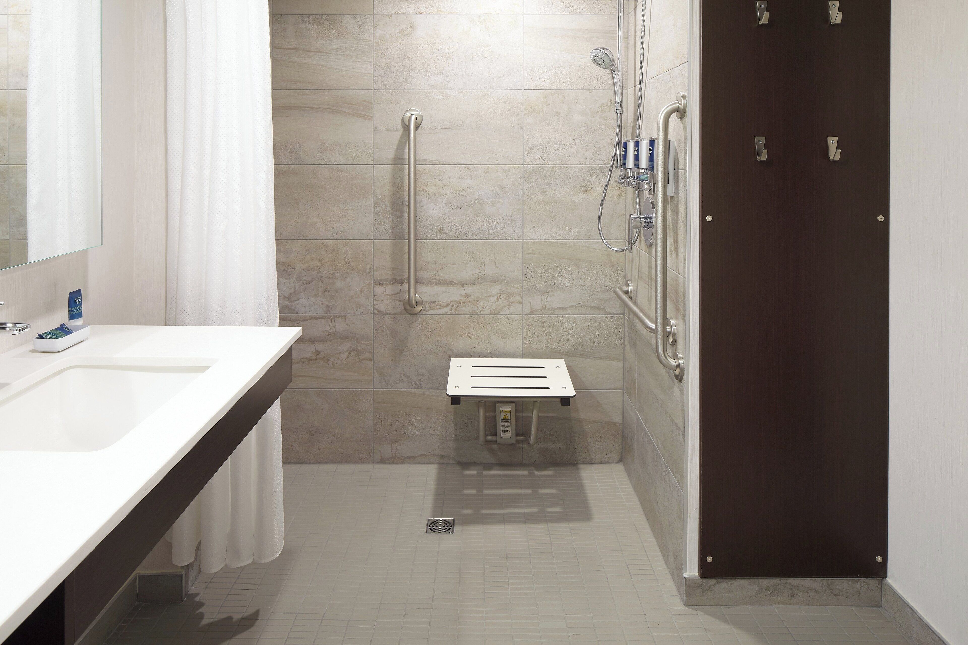 A modern bathroom with a white sink, a shower with a handheld showerhead, and a dark wooden door.