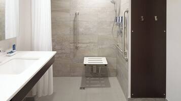 A modern bathroom with a white sink, a shower with a handheld showerhead, and a dark wooden door.