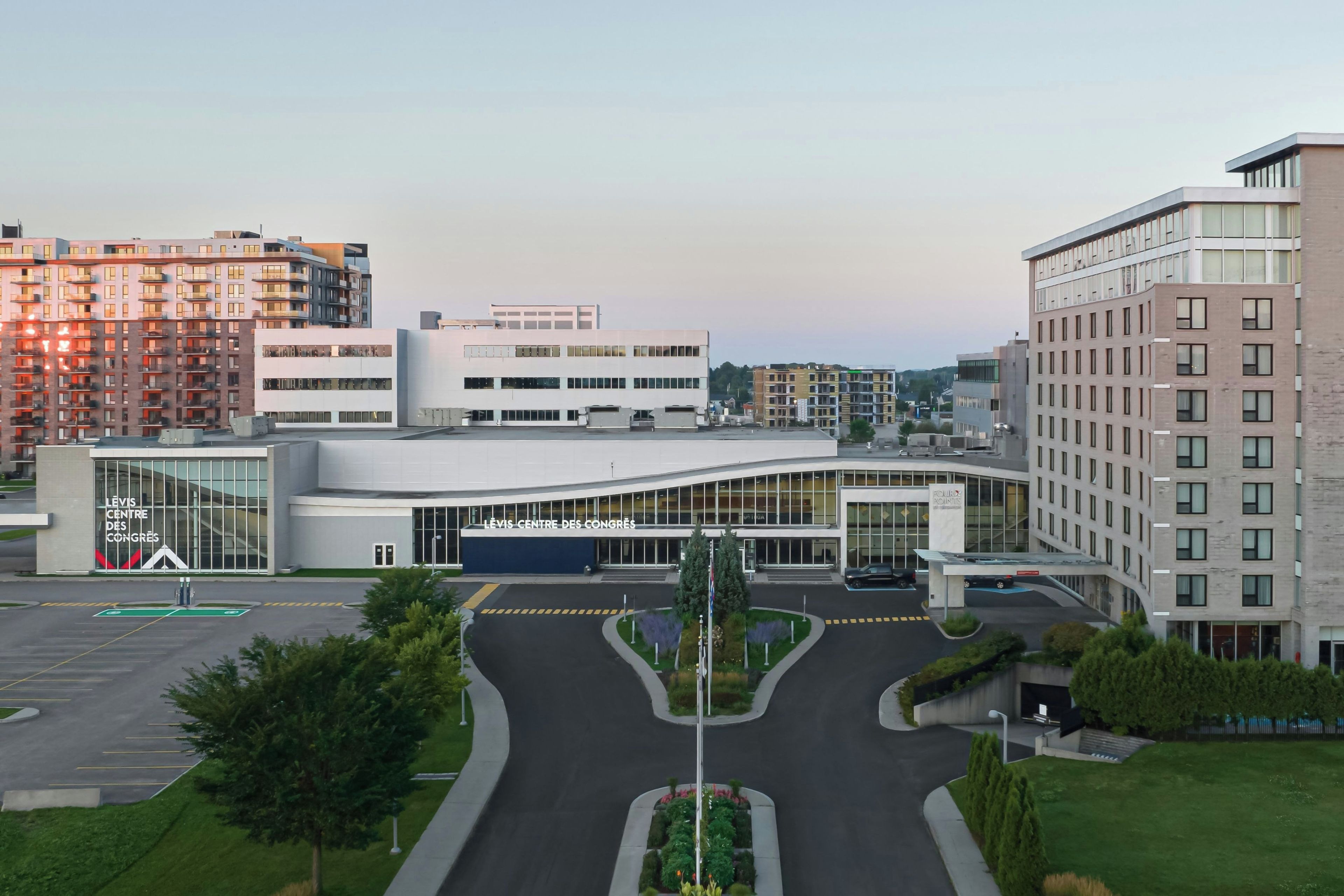 A modern building with a curved facade, a parking lot, and surrounding residential buildings.