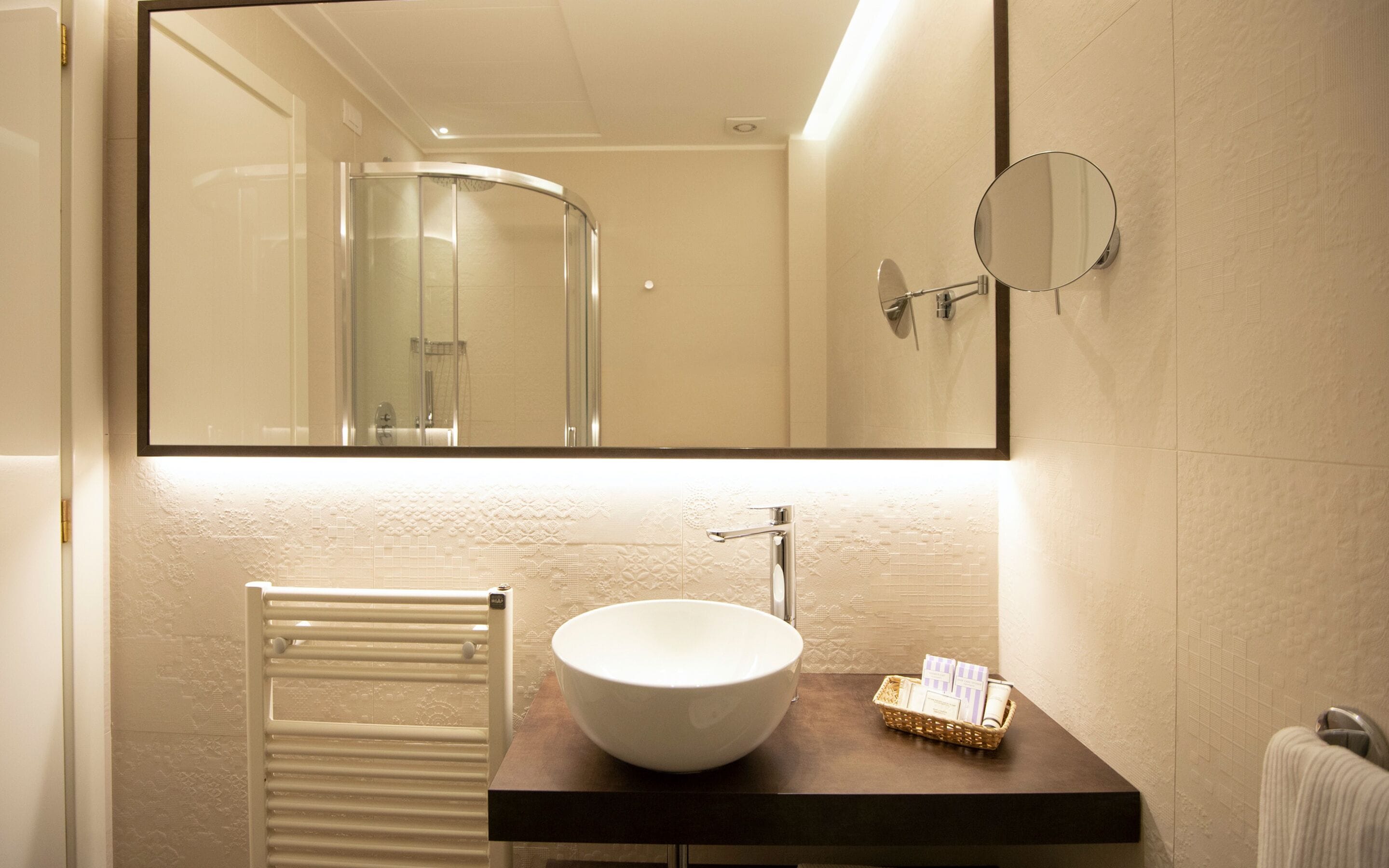 A bathroom with a large mirror, a white sink, a towel rack, and a small basket of toiletries.