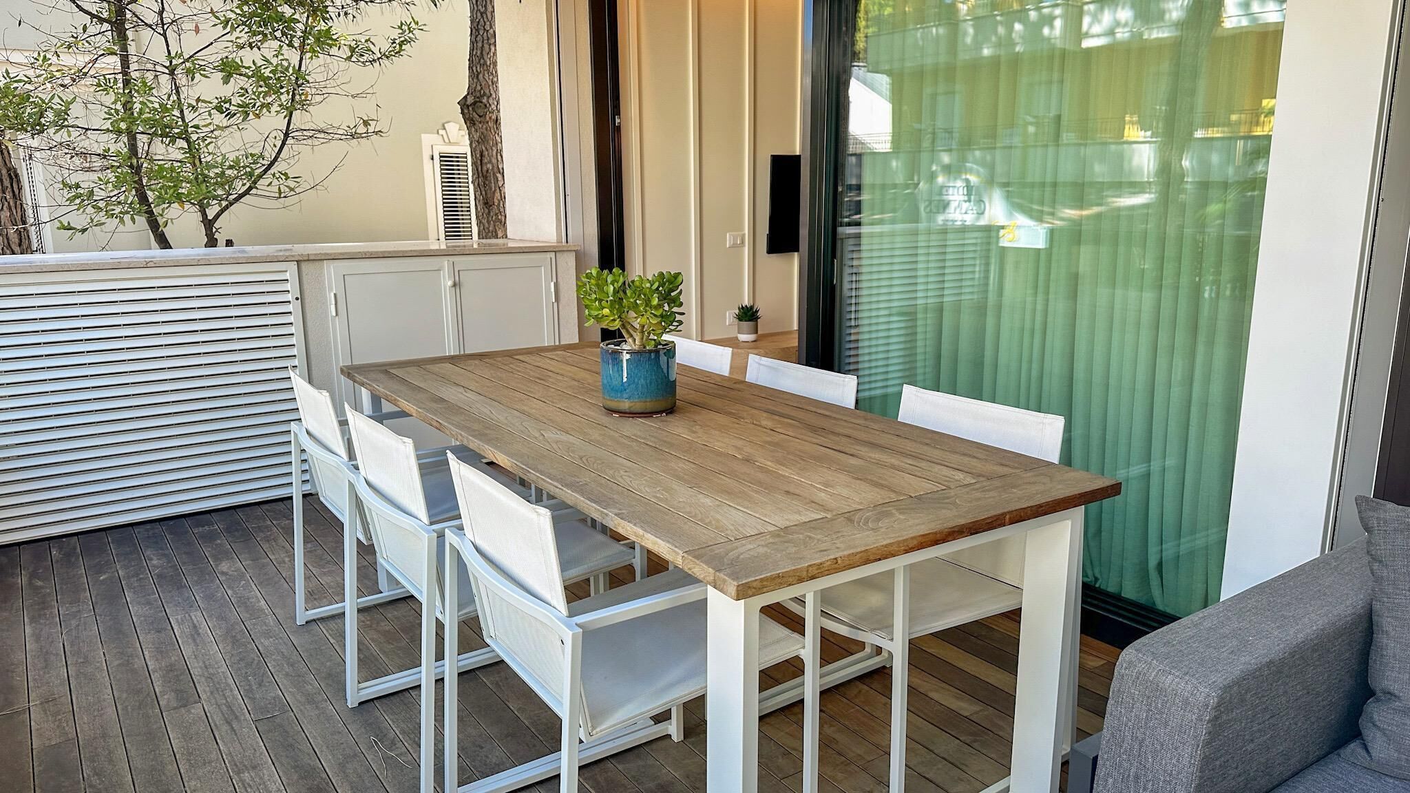 A wooden table with white chairs, a potted plant, and a sliding glass door.