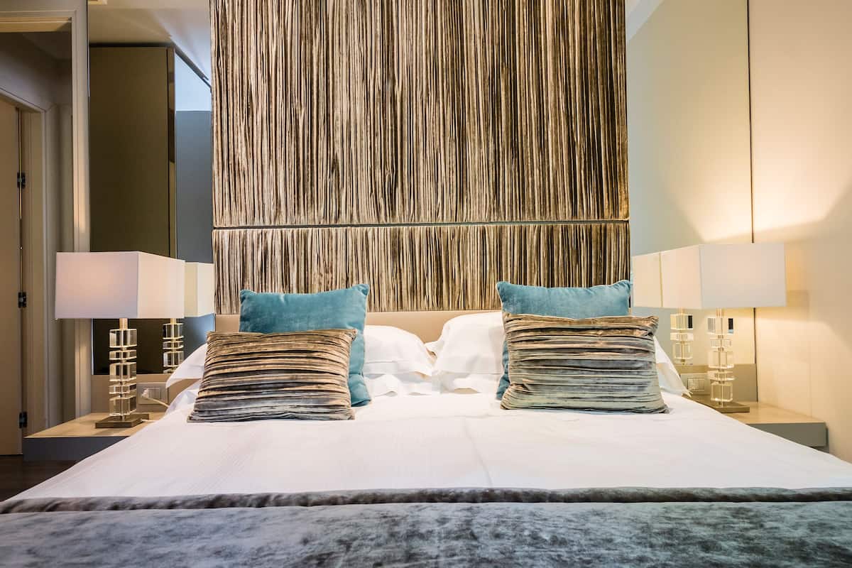 A hotel room with a large bed, two side tables with lamps, a wooden accent wall, and a view of the hallway.