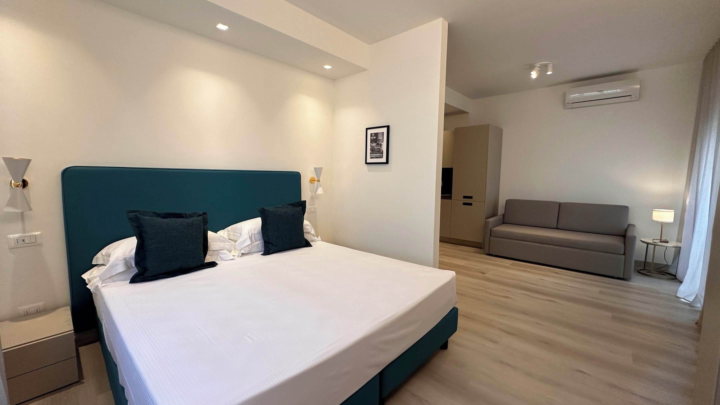 A modern hotel room with a large bed, a sofa, and a small table with a lamp.