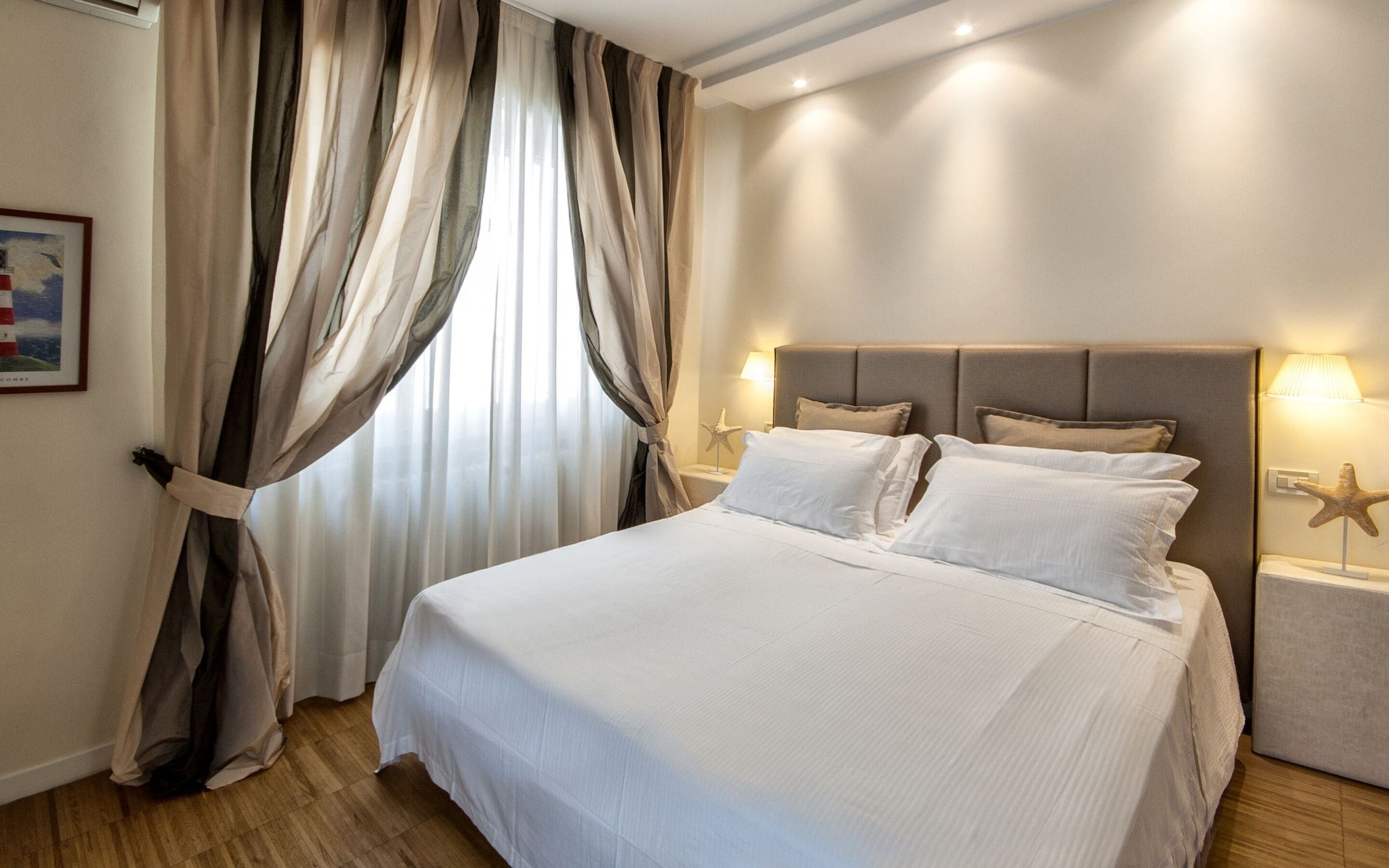 Una habitación de hotel con una cama grande, cortinas color beige, una decoración con forma de estrella de mar y un cuadro en la pared.