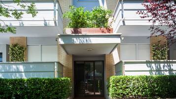 Un edificio moderno con tejado plano, una entrada central con puerta de cristal y un pequeño balcón en lo alto.
