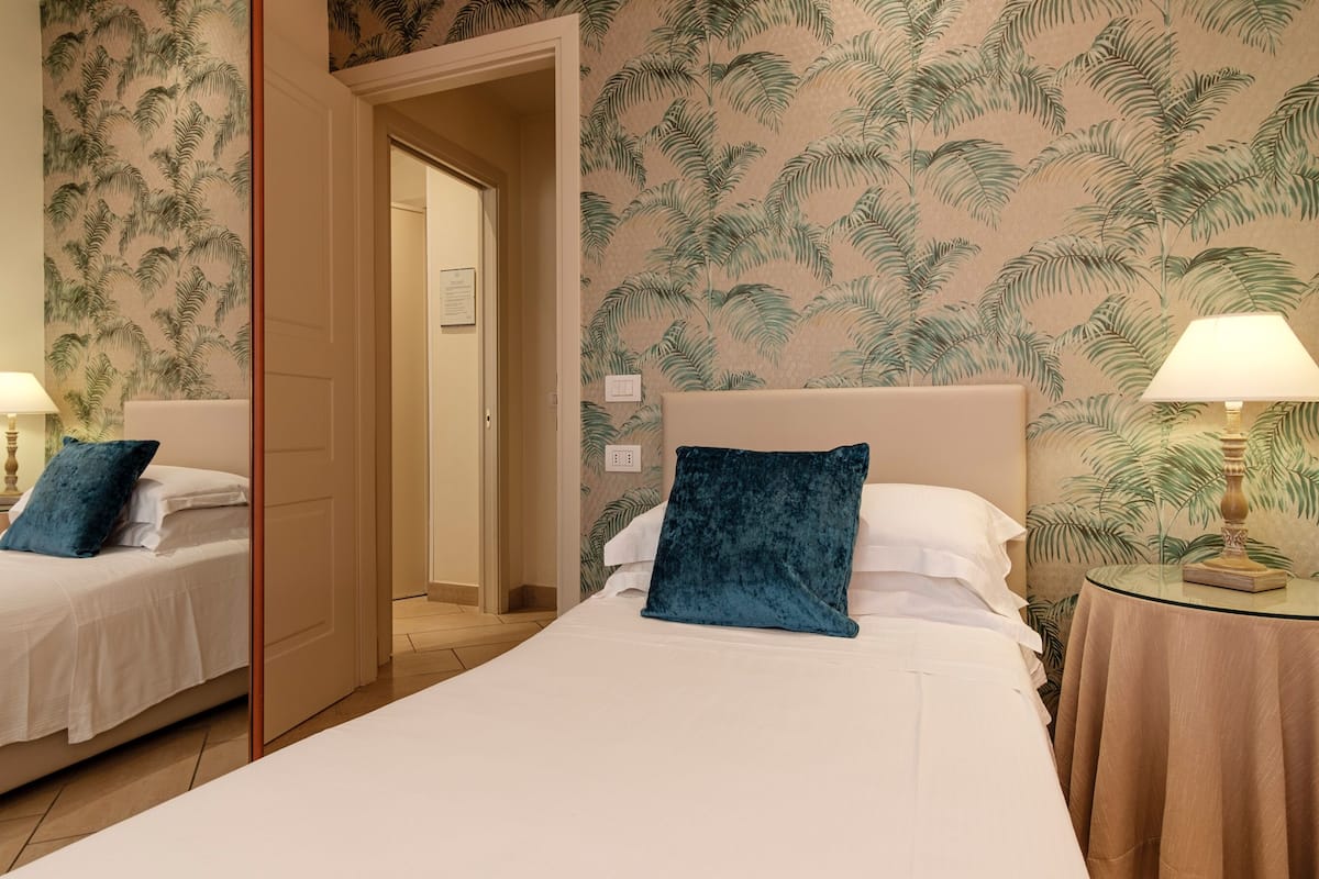 A hotel room with two beds, a mirror, and a nightstand with a lamp.