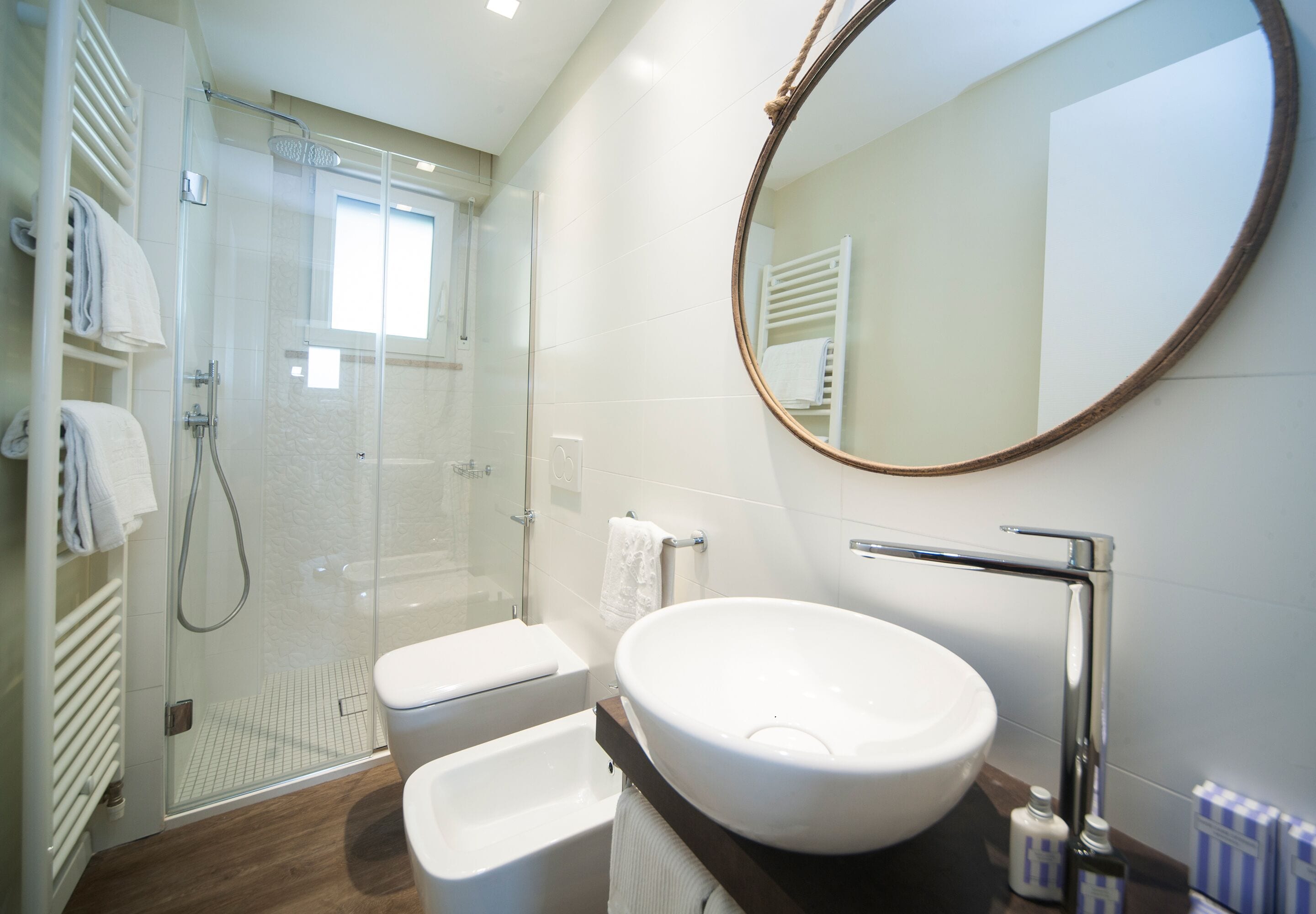 Un baño moderno con ducha de vidrio, un lavabo blanco y un espejo redondo.