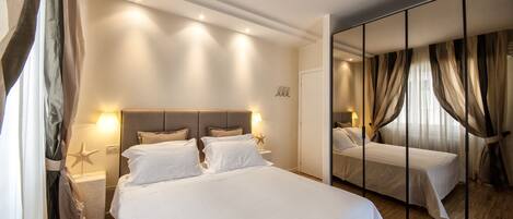 Habitación de hotel con una cama grande, lámparas de noche, una decoración con forma de estrella de mar y un espejo con cortinas.