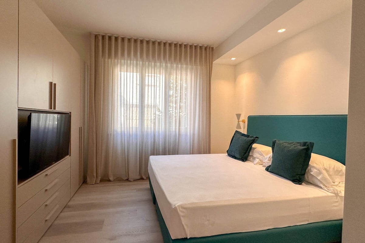A hotel room with a bed, a TV, a window with curtains, and a nightstand.