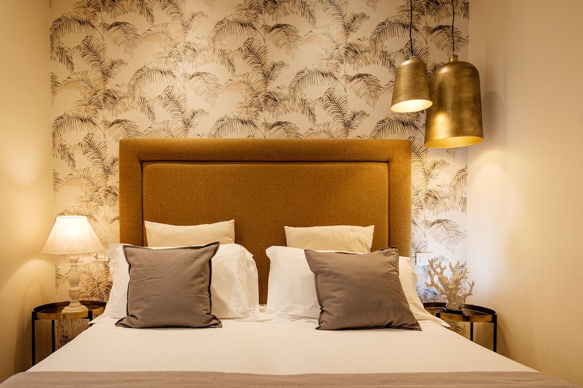 A hotel room with a large bed, two bedside tables, a lamp, and a wall with a leaf pattern.