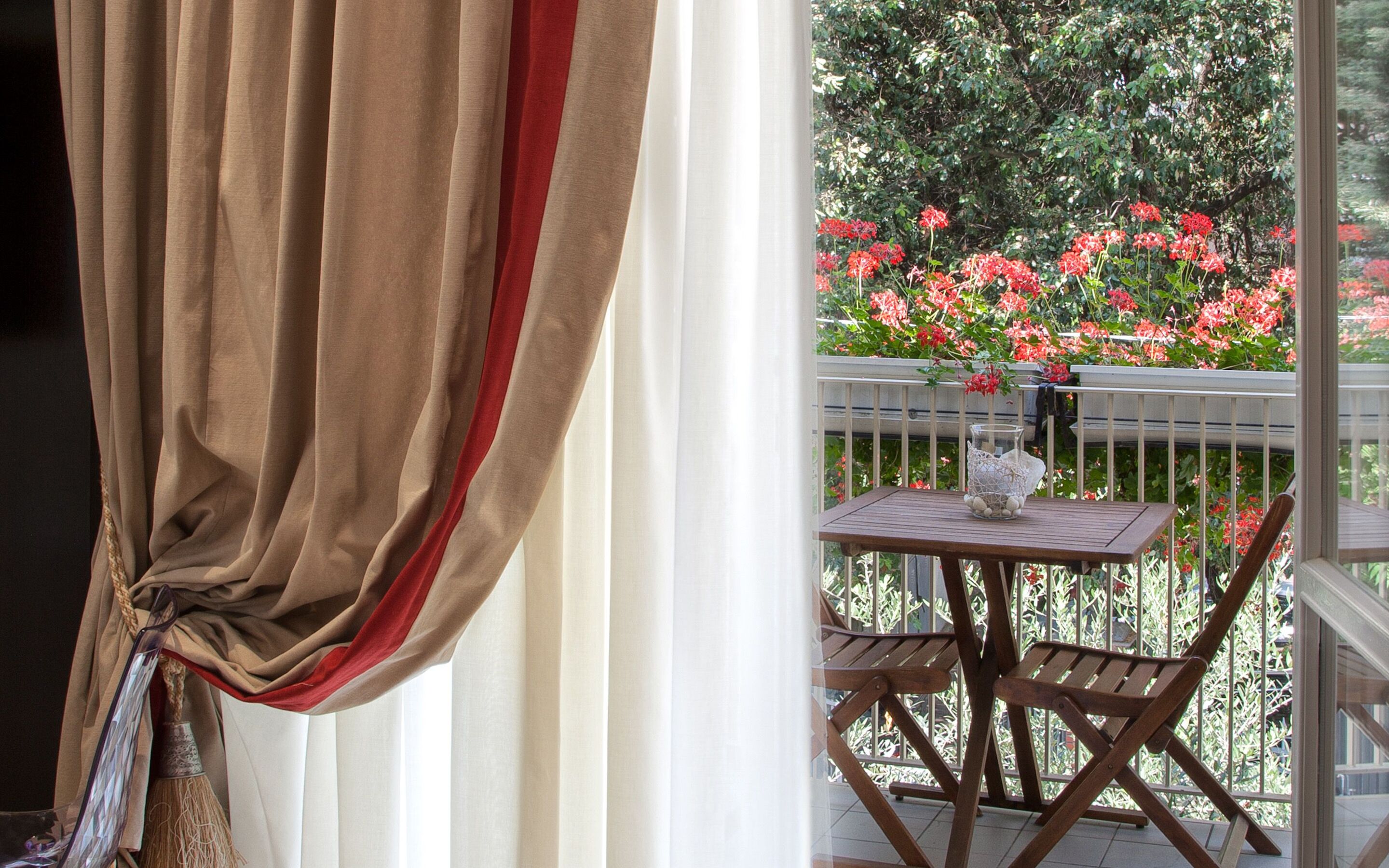Un balcon avec une table et des chaises, une balustrade blanche et des fleurs rouges en arrière-plan.