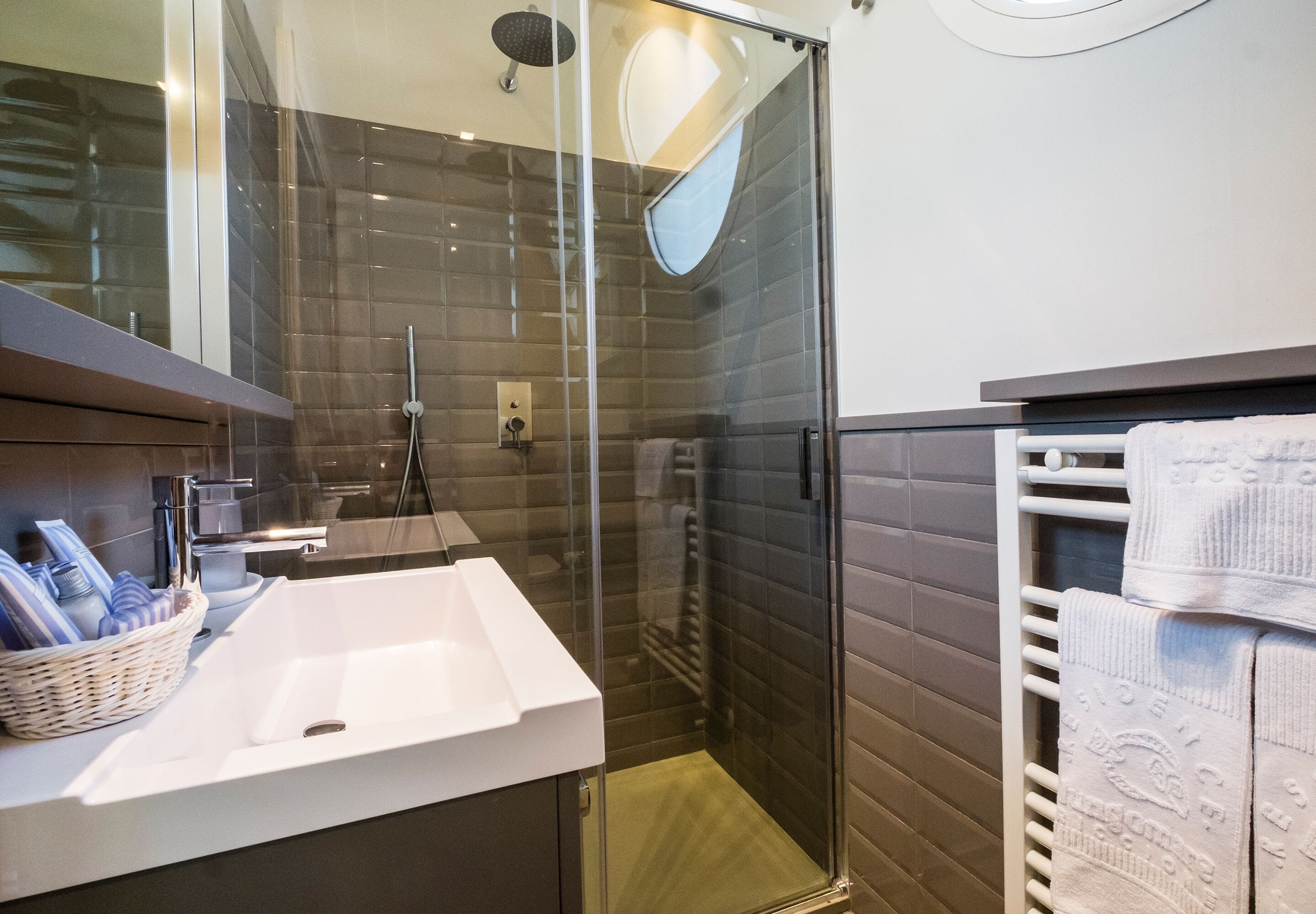 Ein modernes Badezimmer mit einer Glaskabine zur Dusche, einem weißen Waschbecken und einem Handtuchhalter mit ordentlich gefalteten Handtüchern.