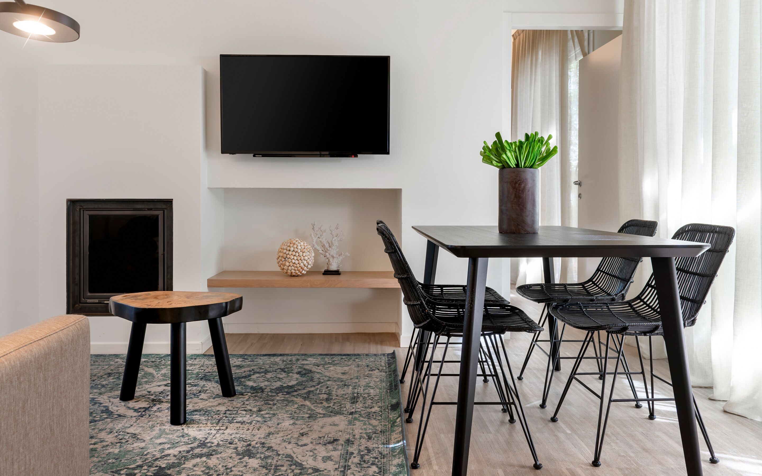 A modern living room with a flat-screen TV, a dining table with chairs, a sofa, a decorative plant, and a fireplace.