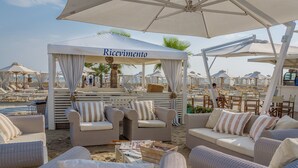 Un área de descanso frente a la playa con mobiliario de mimbre, un bar y sombrillas.