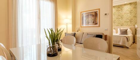 A hotel room with a dining area, a sofa, a bed, and a painting on the wall.