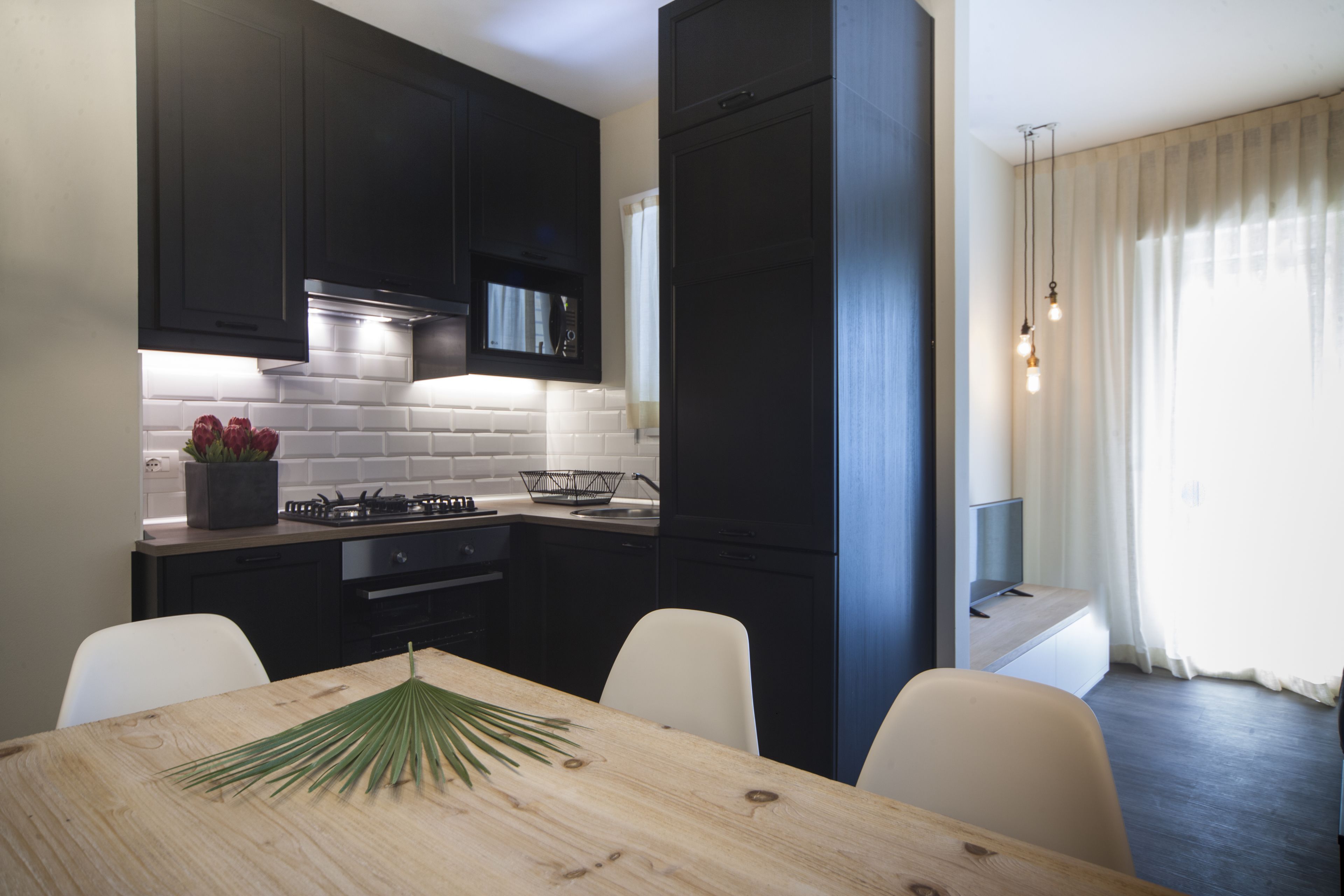 A modern kitchen with dark cabinetry, a wooden dining table, and a built-in stove.