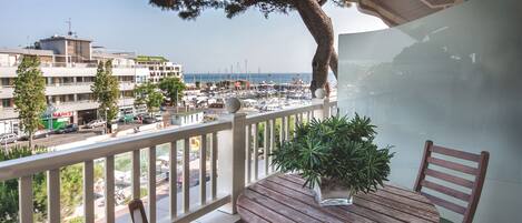 A balcony with a wooden table and chairs, overlooking a marina with boats and a cityscape.