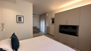 Habitación de hotel con una cama grande, un televisor y una zona de estar con sofá y cortinas.