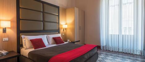 Une chambre d’hôtel avec un grand lit, une table de chevet avec un téléphone, une armoire et une fenêtre avec des rideaux légers.