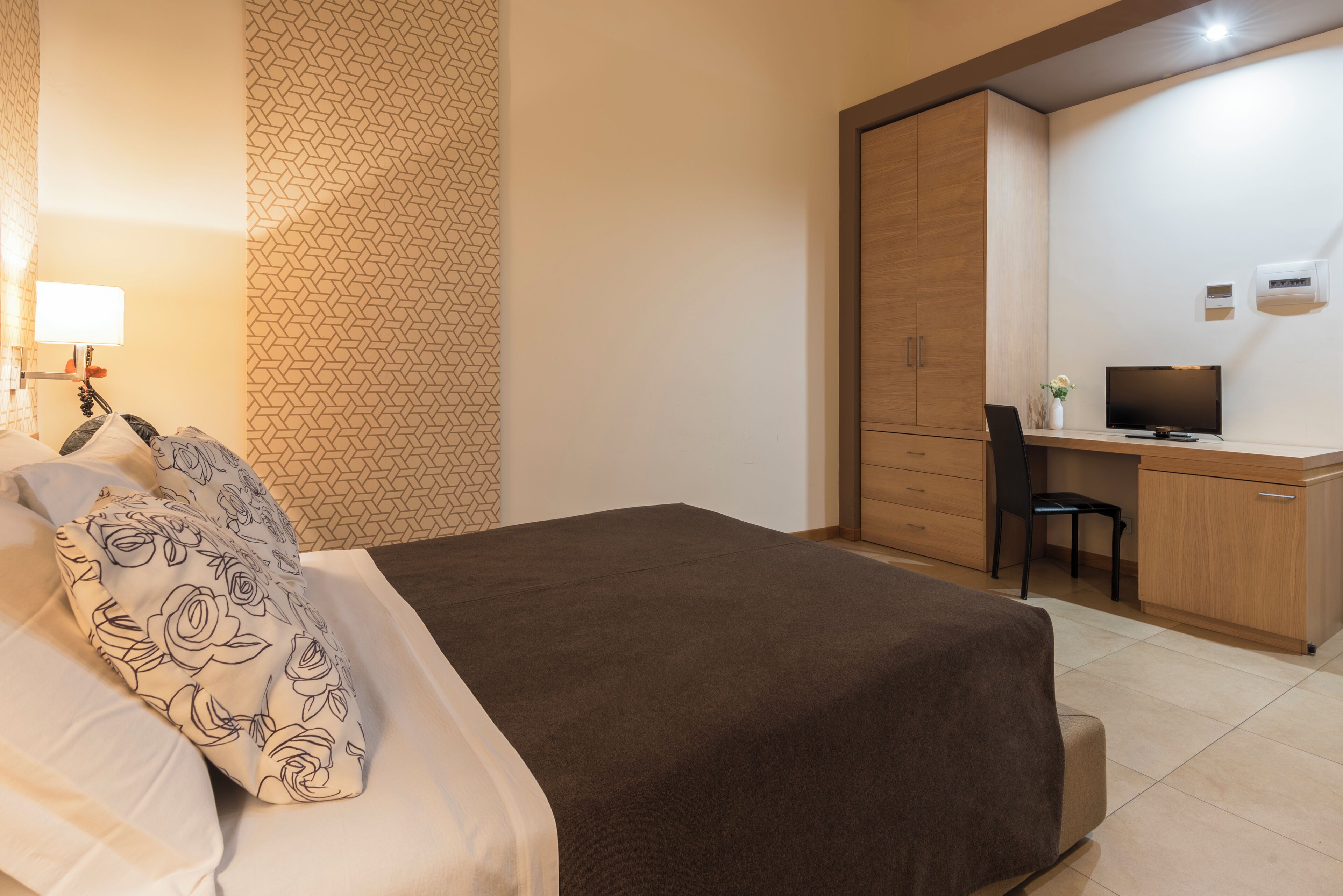A neatly arranged bedroom with a bed, a desk, a chair, and a television.
