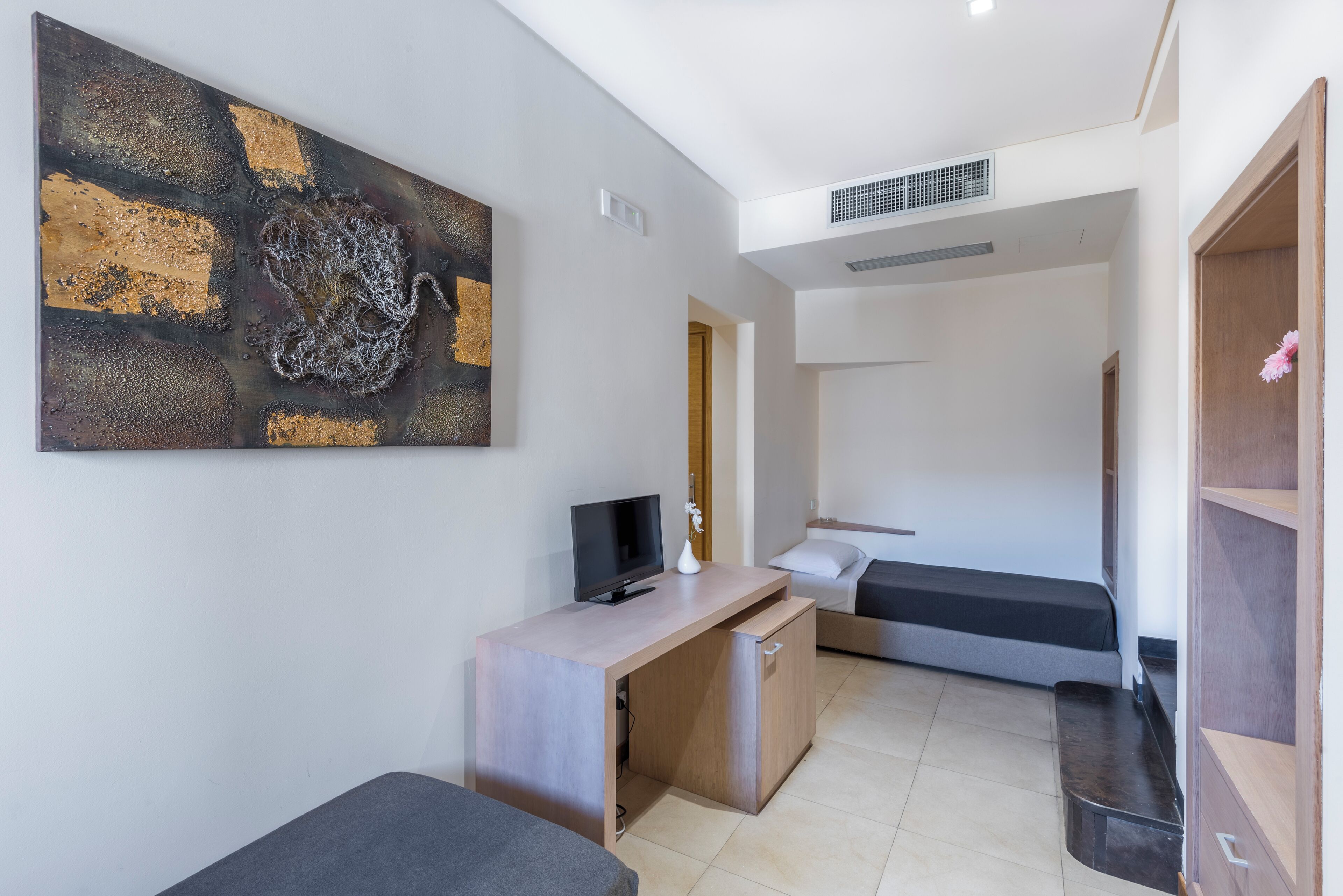 A compact room with a bed, a desk with a television, and a large abstract painting on the wall.
