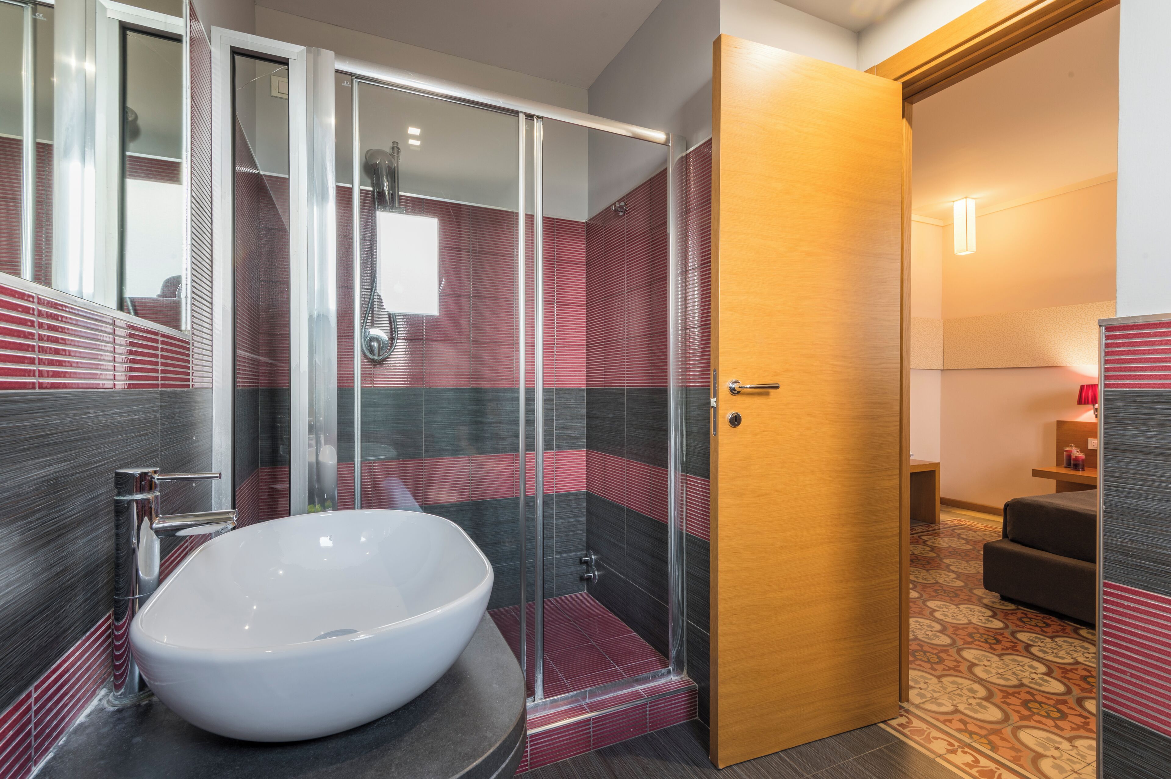 Een moderne badkamer met een grote witte wastafel, een glazen douchecabine en een houten deur naar een slaapkamer.